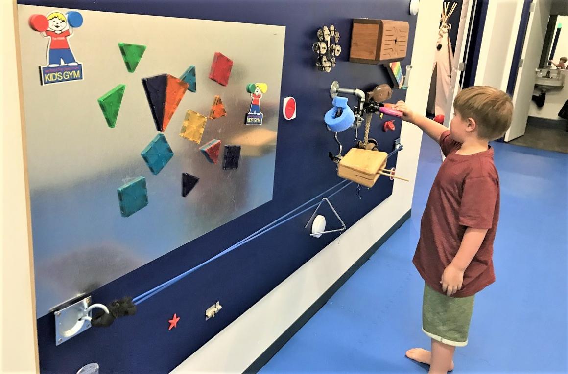 A boy stands and plays with a wall of toys at We Rock the Spectrum an inclusive sensory sensitive play gym in Federal Way near Seattle